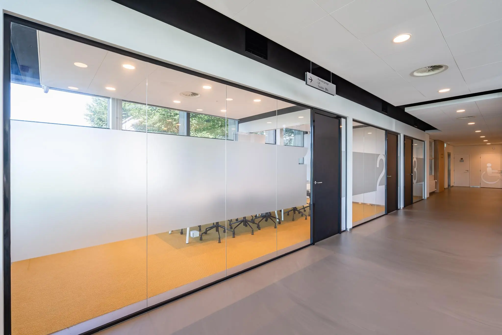 Moderne kantoorruimte aan de Rivium Promenade met glazen vergaderruimtes en genummerde deuren langs een brede gang.